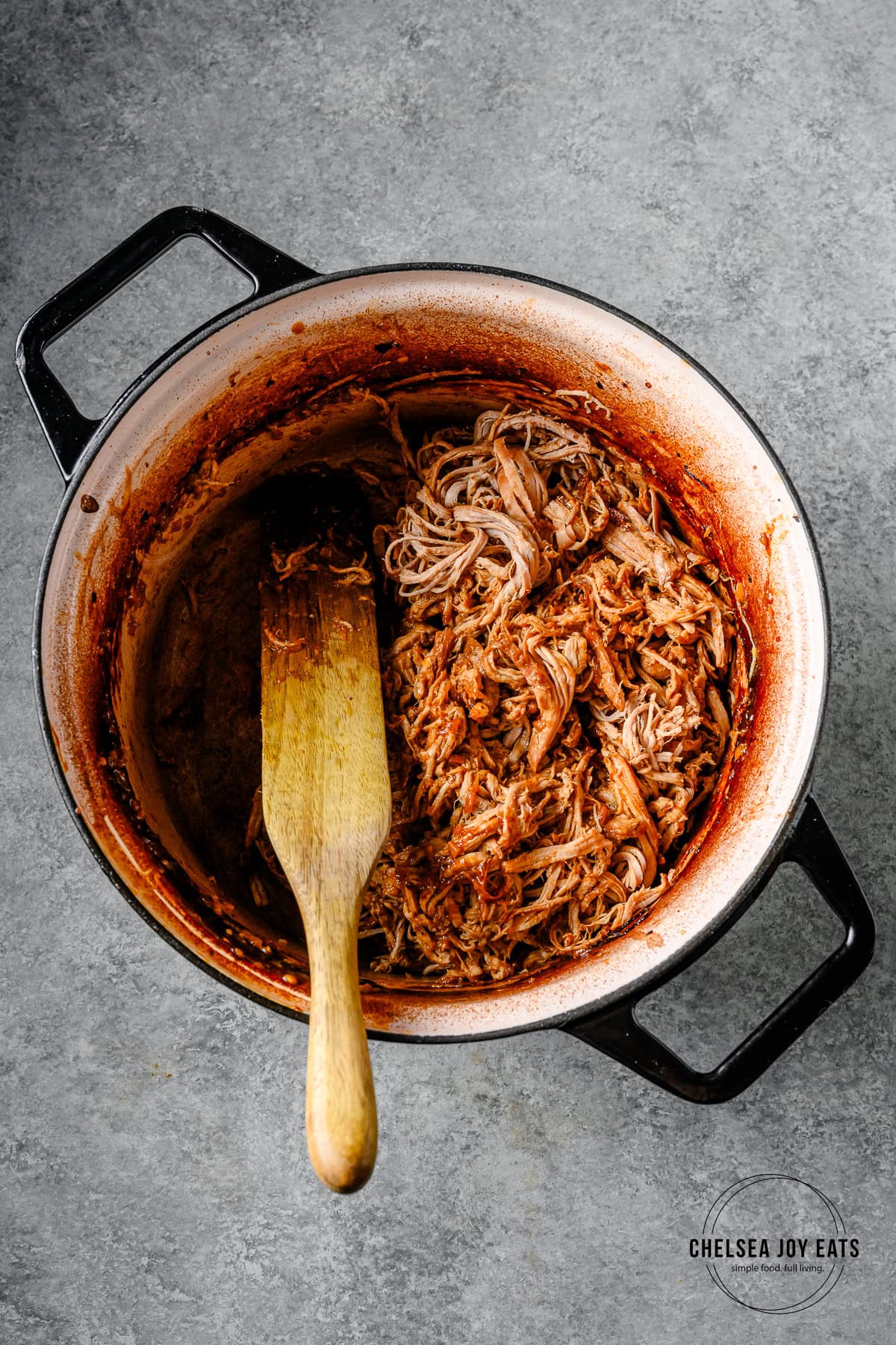 Shredded pork tenderloin stirred with a miso orange sauce in a Dutch oven with a wooden spoon.