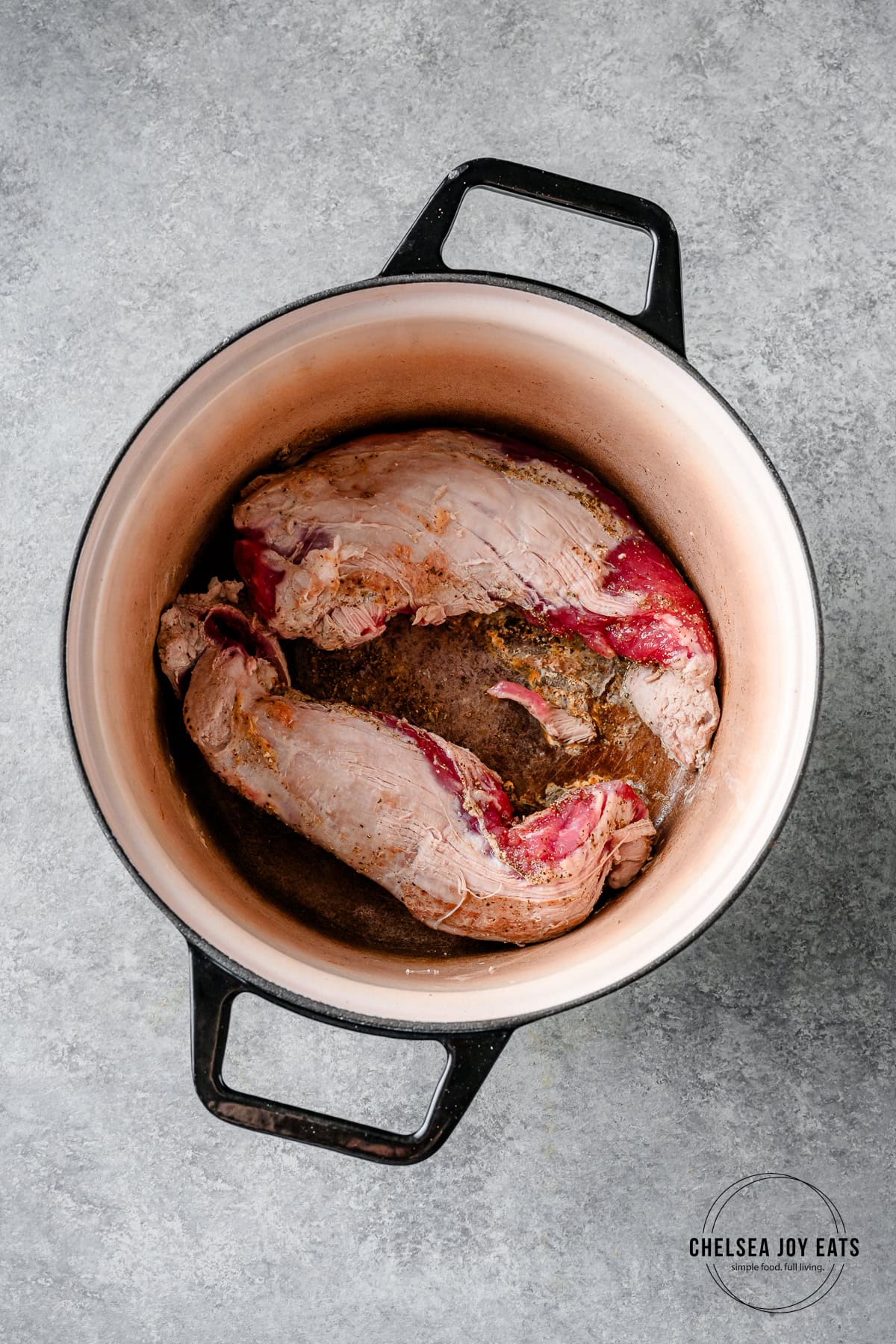 Two pork tenderloins searing in a Dutch oven.