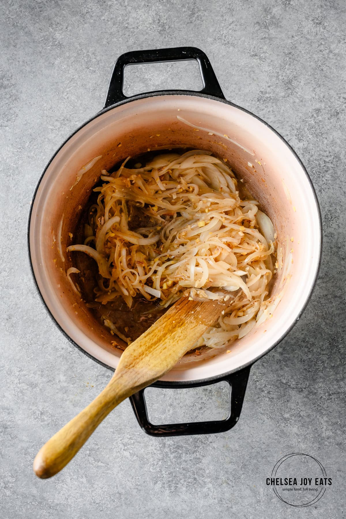 Onions, garlic, and ginger sauteing in a Dutch oven with a wooden spoon stirring.