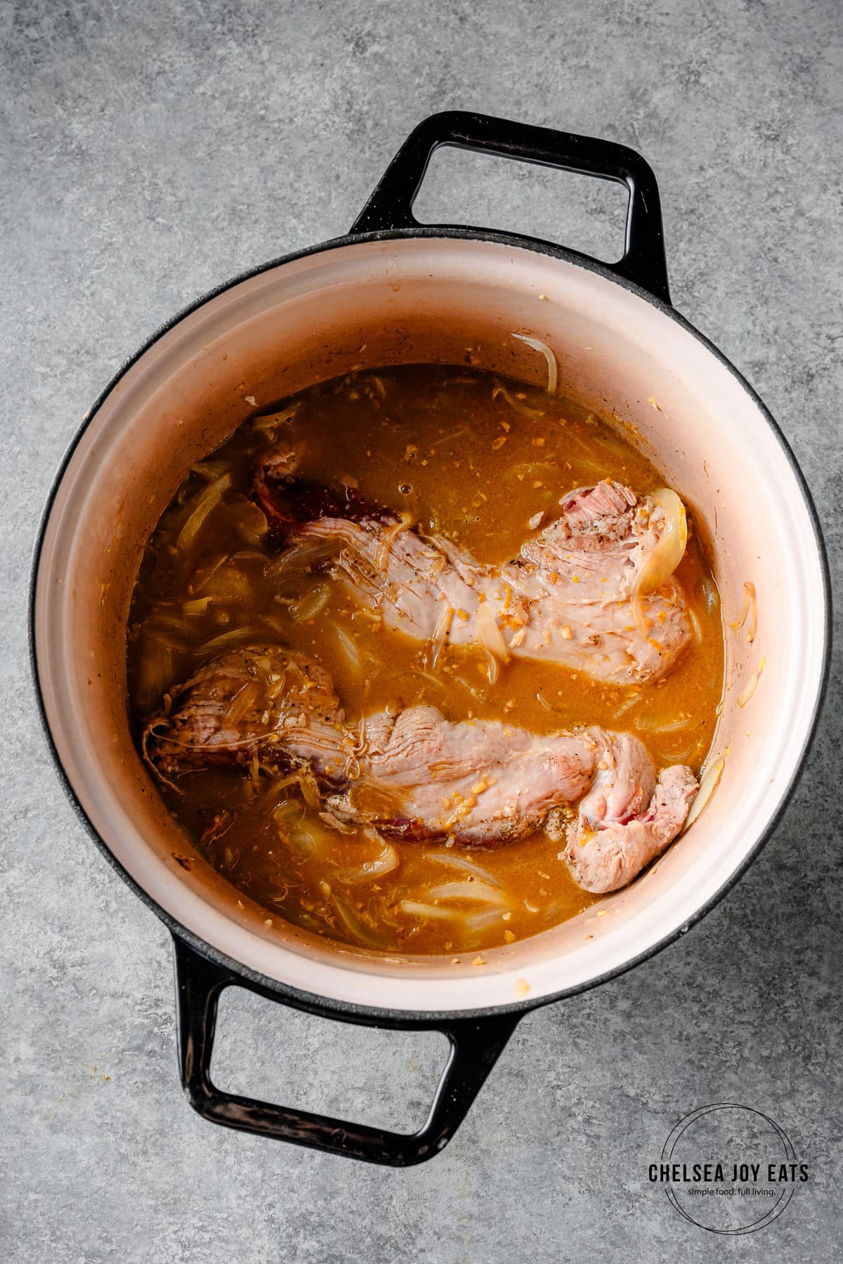 Dutch oven with partially cooked pork tenderloin and a miso orange braising liquid, ready for the oven.