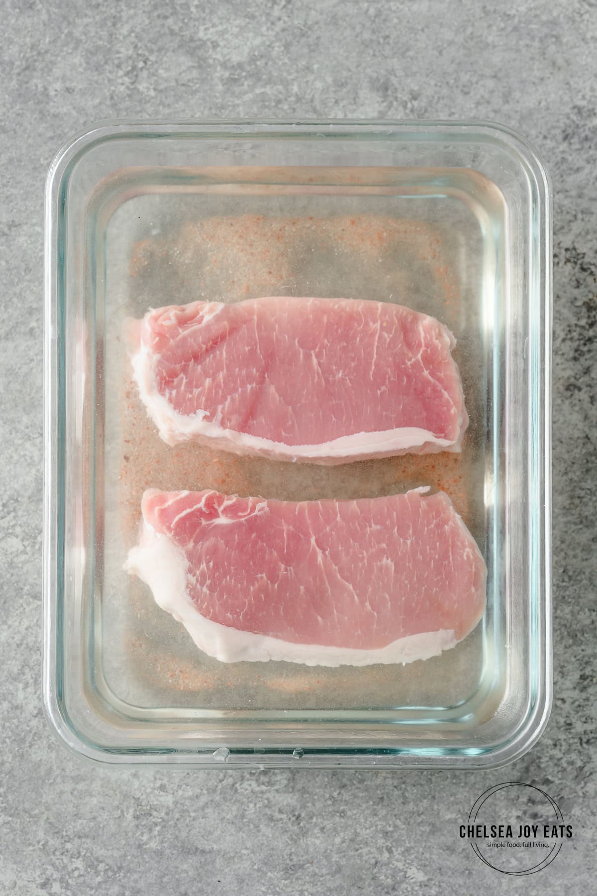 Pork chops brining in a glass dish with water and salt.