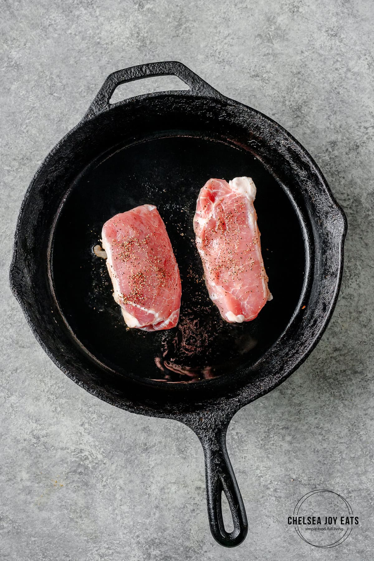 Pork chops cooking in a cast iron skillet.