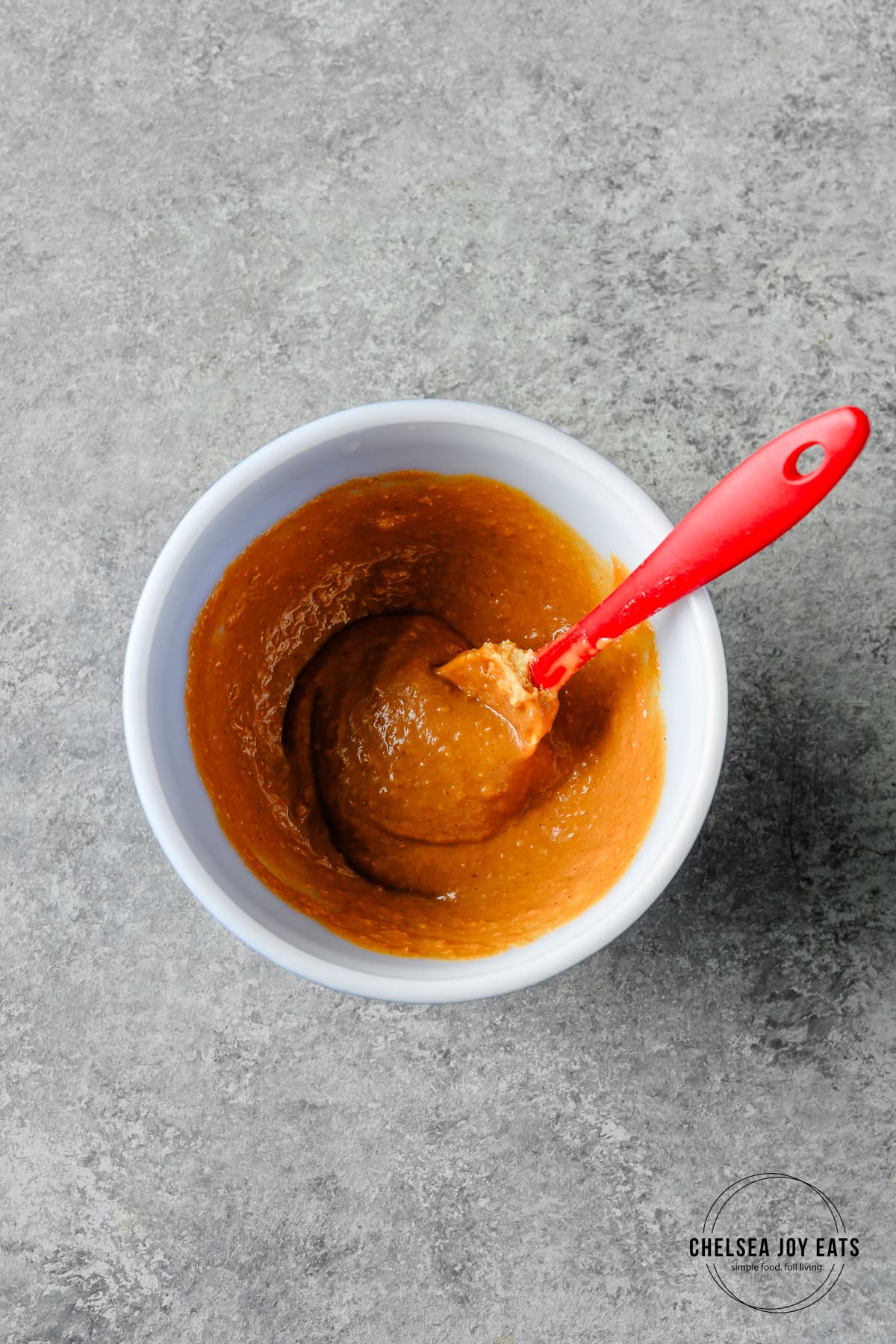 Stirred peanut sauce in a small cermaic bowl with a spatula.