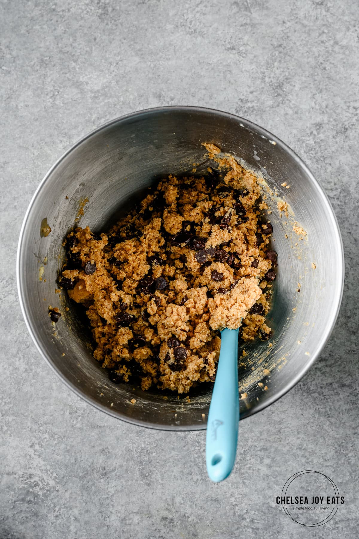 Cookie dough for gluten free tahini chocolate chip cookies in the bowl of a stand mixer with a spatula.