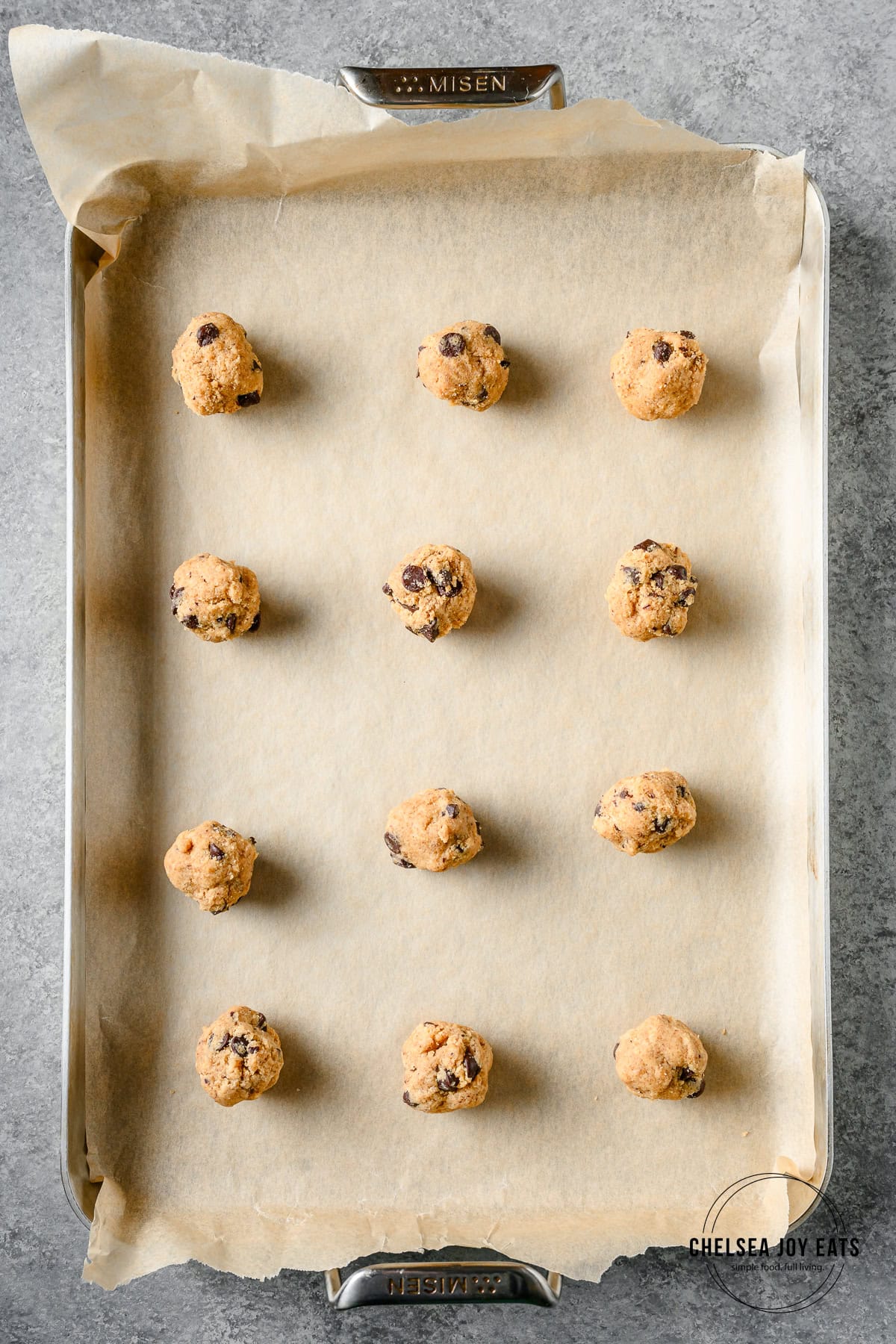 Balls of gluten free tahini chocolate chip cookie dough ready to bake on a parchment paper lined baking sheet.