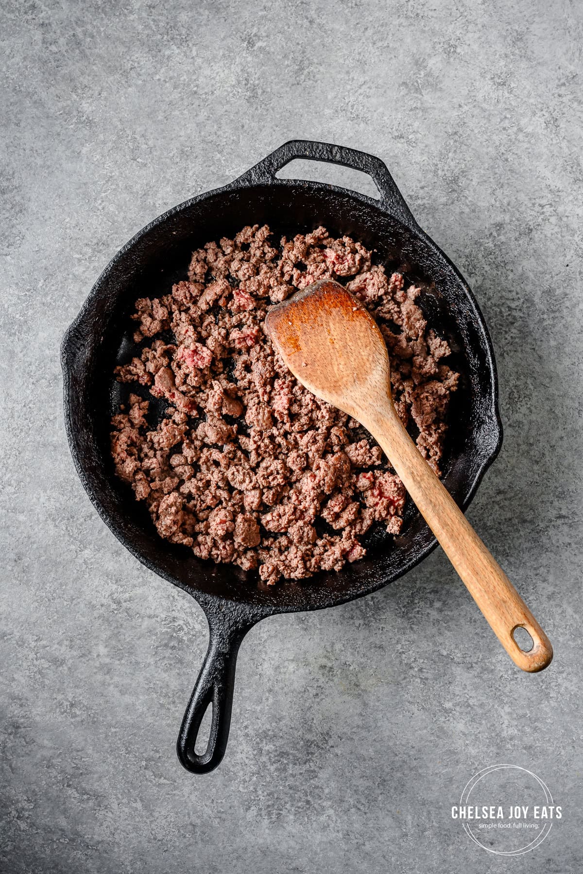 Browned ground beef in a cast iron skillet with a wooden spatula.