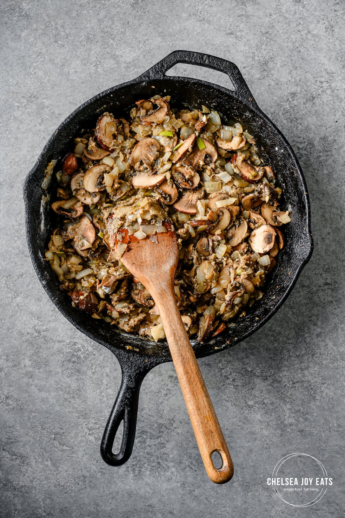 Sautéed mushrooms and onions with a roux in a cast iron skilelt with a wooden spatula.