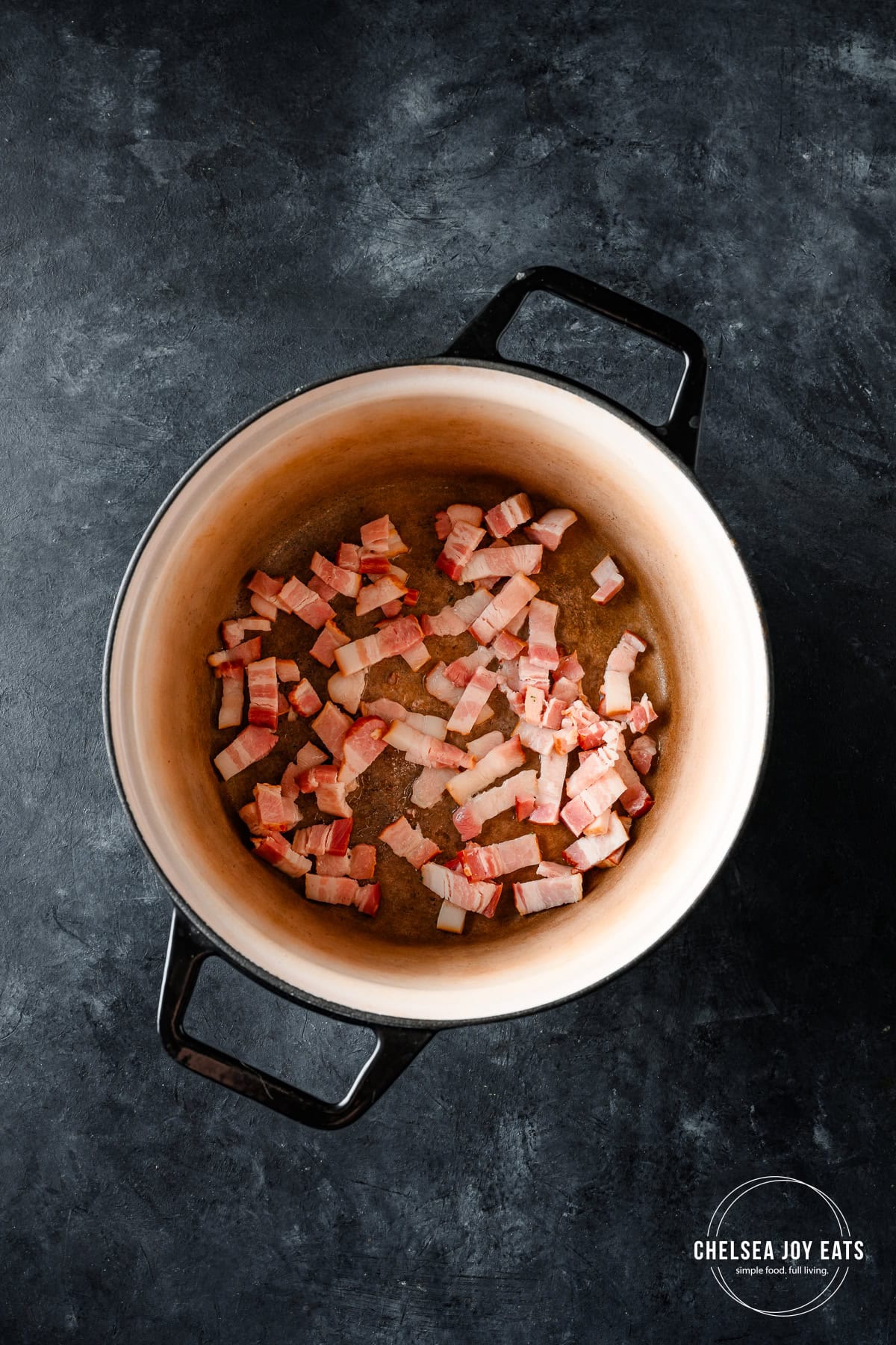 Bacon cooking in a Dutch oven on a dark countertop.