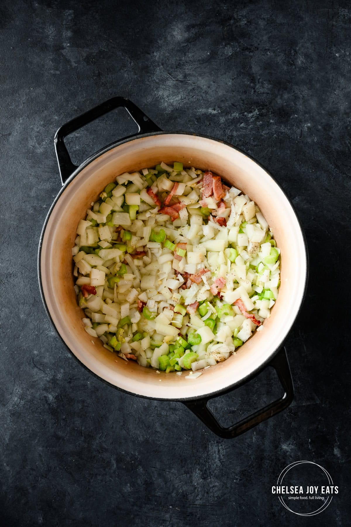 Celery and onion sauteing in a Dutch oven on a dark background.