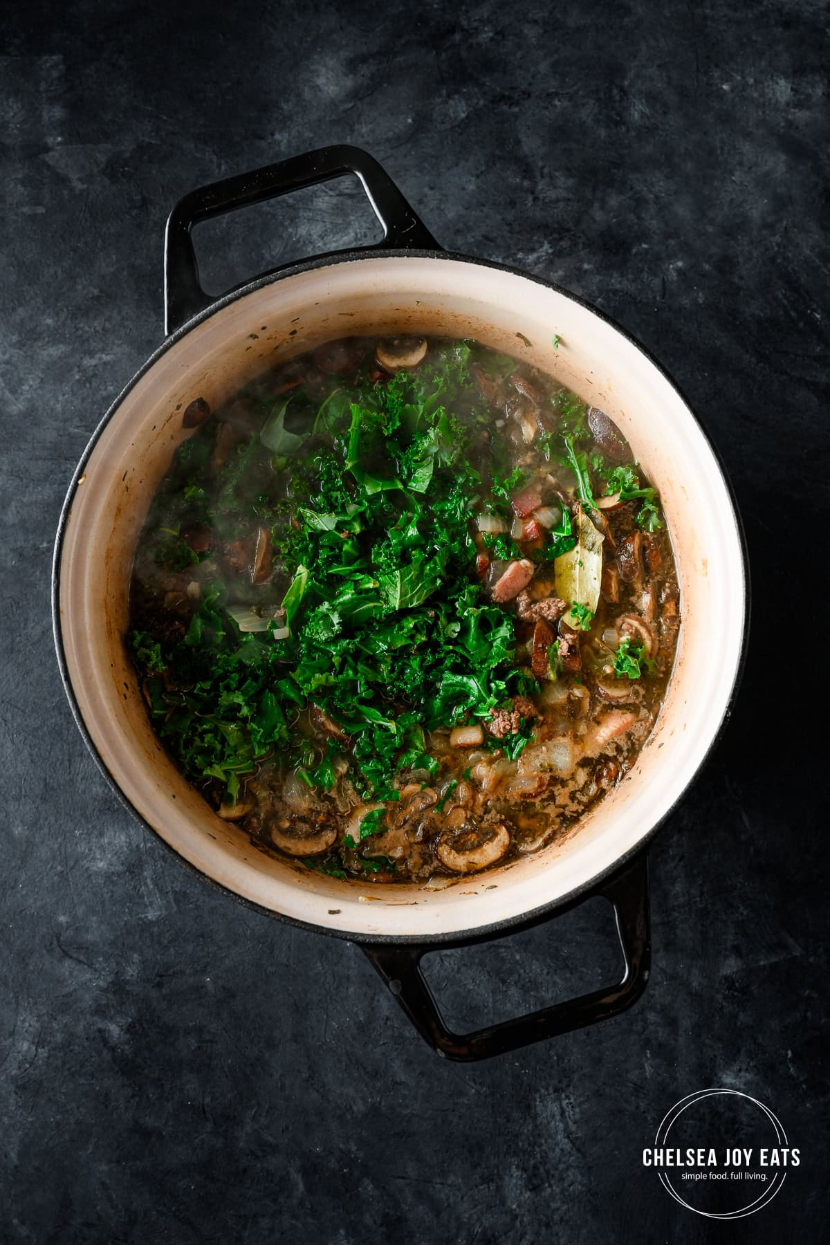 Kale added to a Dutch oven with bacon, bison, and mushroom soup simmering.