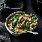 Bowl of bacon bison mushroom soup with kale and a spoon in the soup.