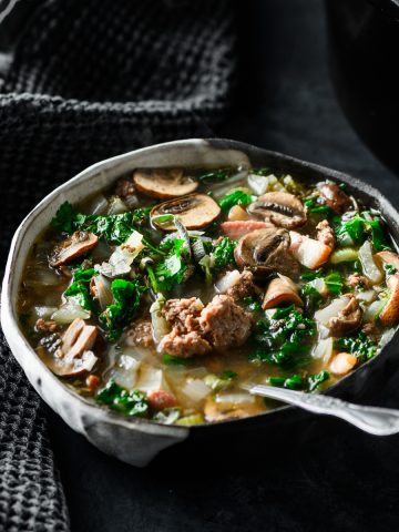 Bowl of bacon bison mushroom soup with kale and a spoon in the soup.