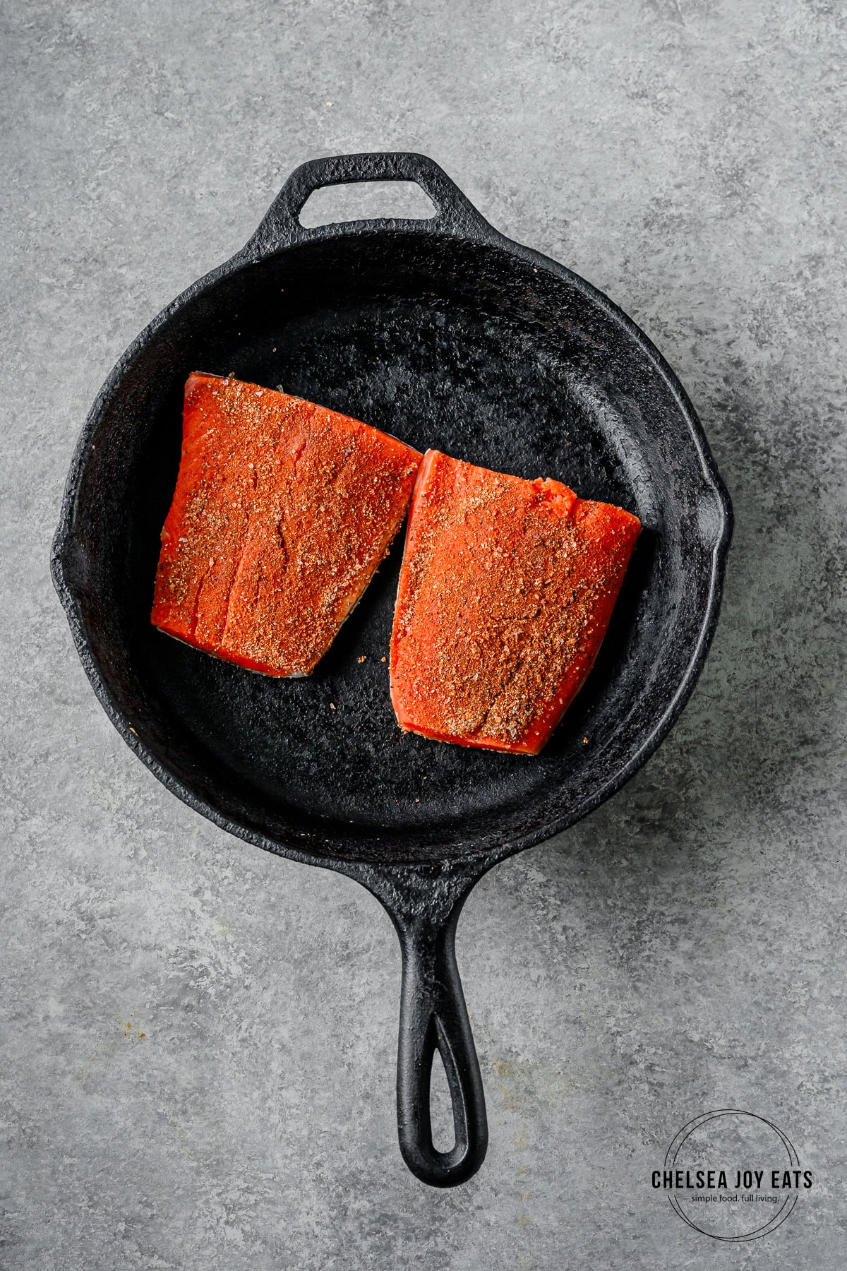 Two seasoned salmon fillets cooking skin side down in a cast iron skillet.