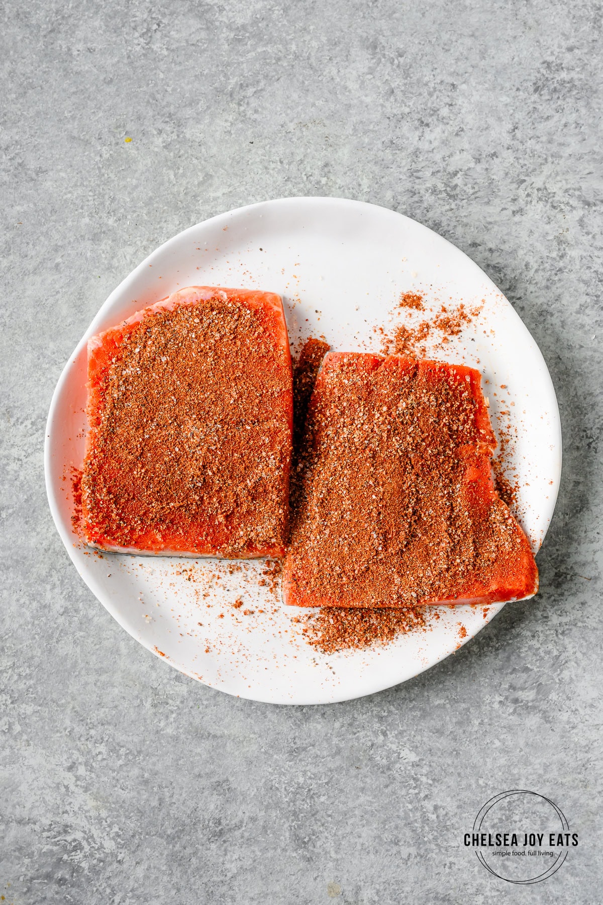 Two seasoned salmon portions on a white ceramic plate.