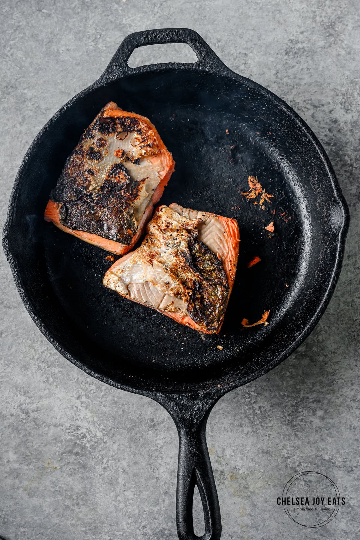 Two salmon fillets cooking flesh side down in a cast iron skillet.
