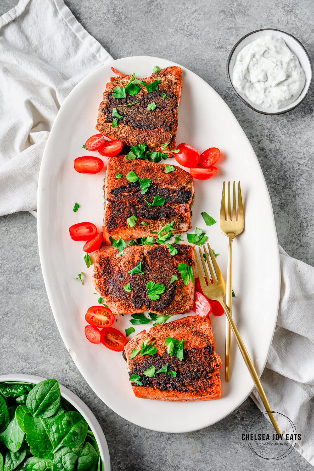 White ceramic platter with 4 blackened salmon fillets garnished with parsley and grape tomato halves.