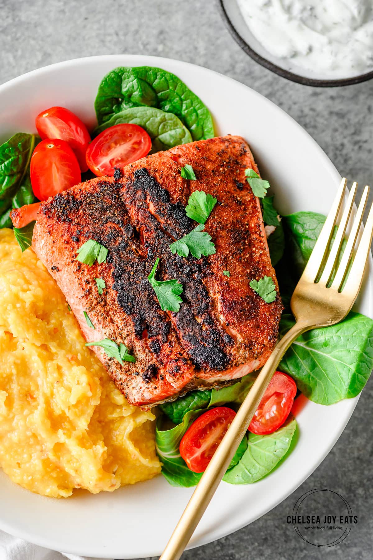 Blackened crispy skin salmon served over greens and polenta in a shallow bowl with a fork alongside.