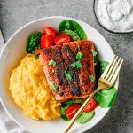 Gluten free blackened salmon served in a shallow bowl over polenta and greens.