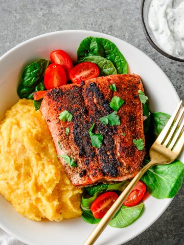 Gluten free blackened salmon served in a shallow bowl over polenta and greens.