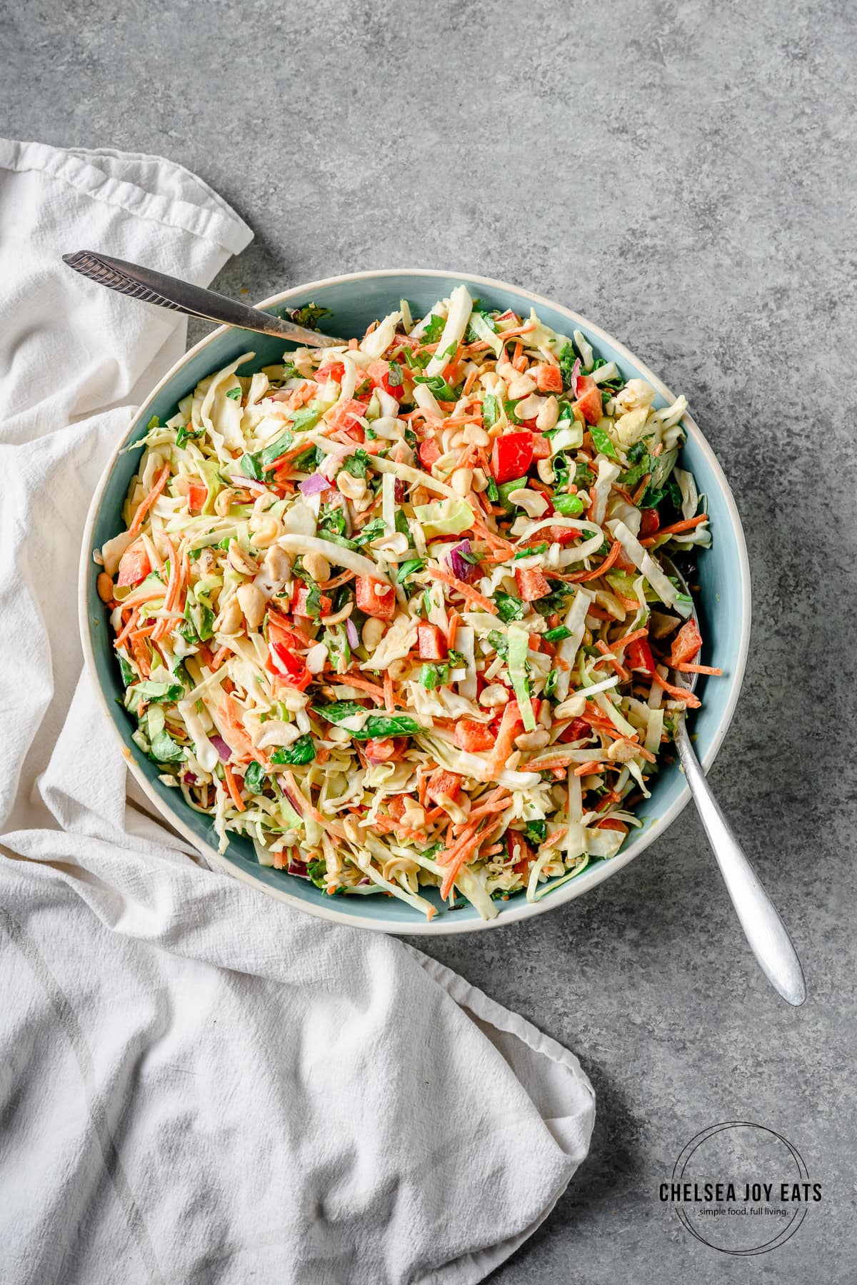 Thai Cabbage Salad tossed in dressing in a large ceramic bowl with metal utensils.