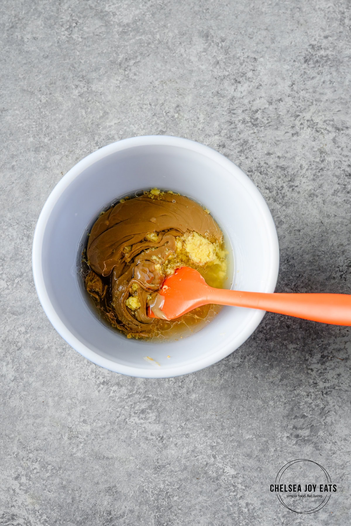 Thai peanut salad dressing ingredients in a small ceramic bowl with a silicone spatula.