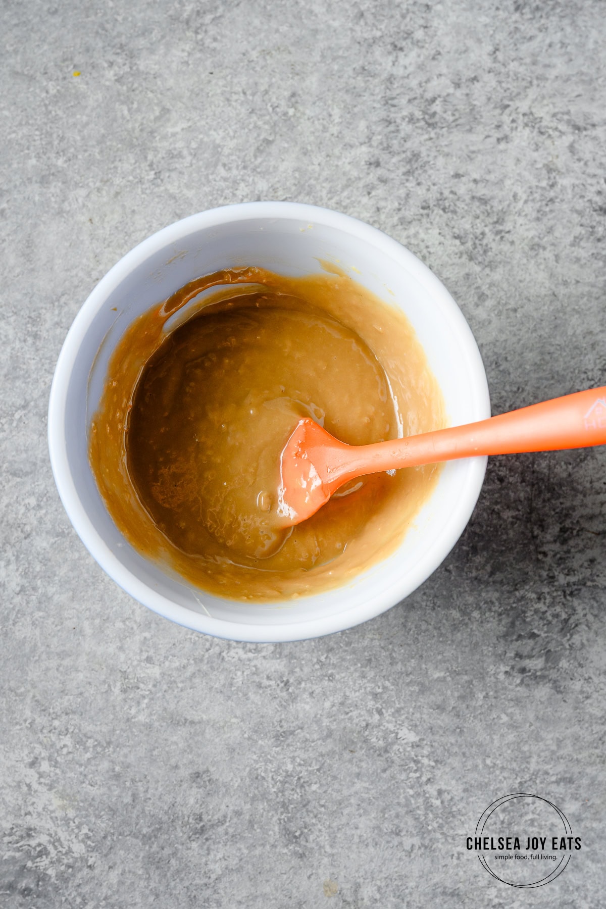 Thai peanut salad dressing ingredients in a small ceramic bowl, blended together with a silicone spatula.