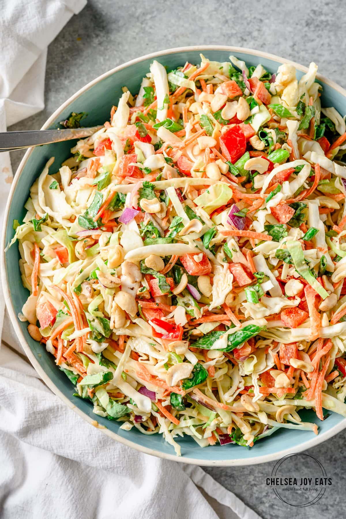 Thai cabbage salad with red bell pepper, red onion, and fresh herbs tossed with a sunflower butter dressing in a large ceramic bowl.