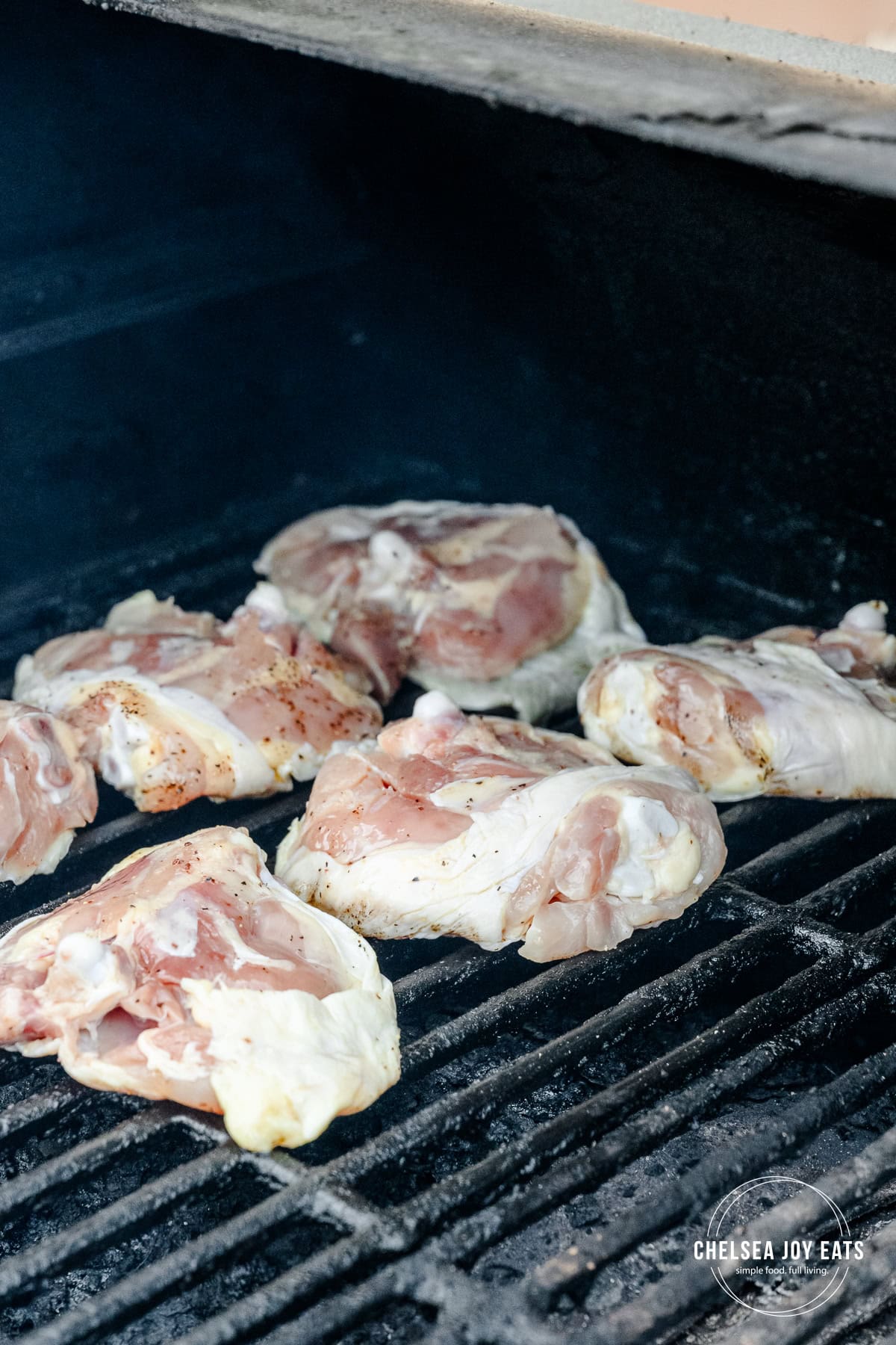 Chicken thighs cooking on a grill, skin side down.