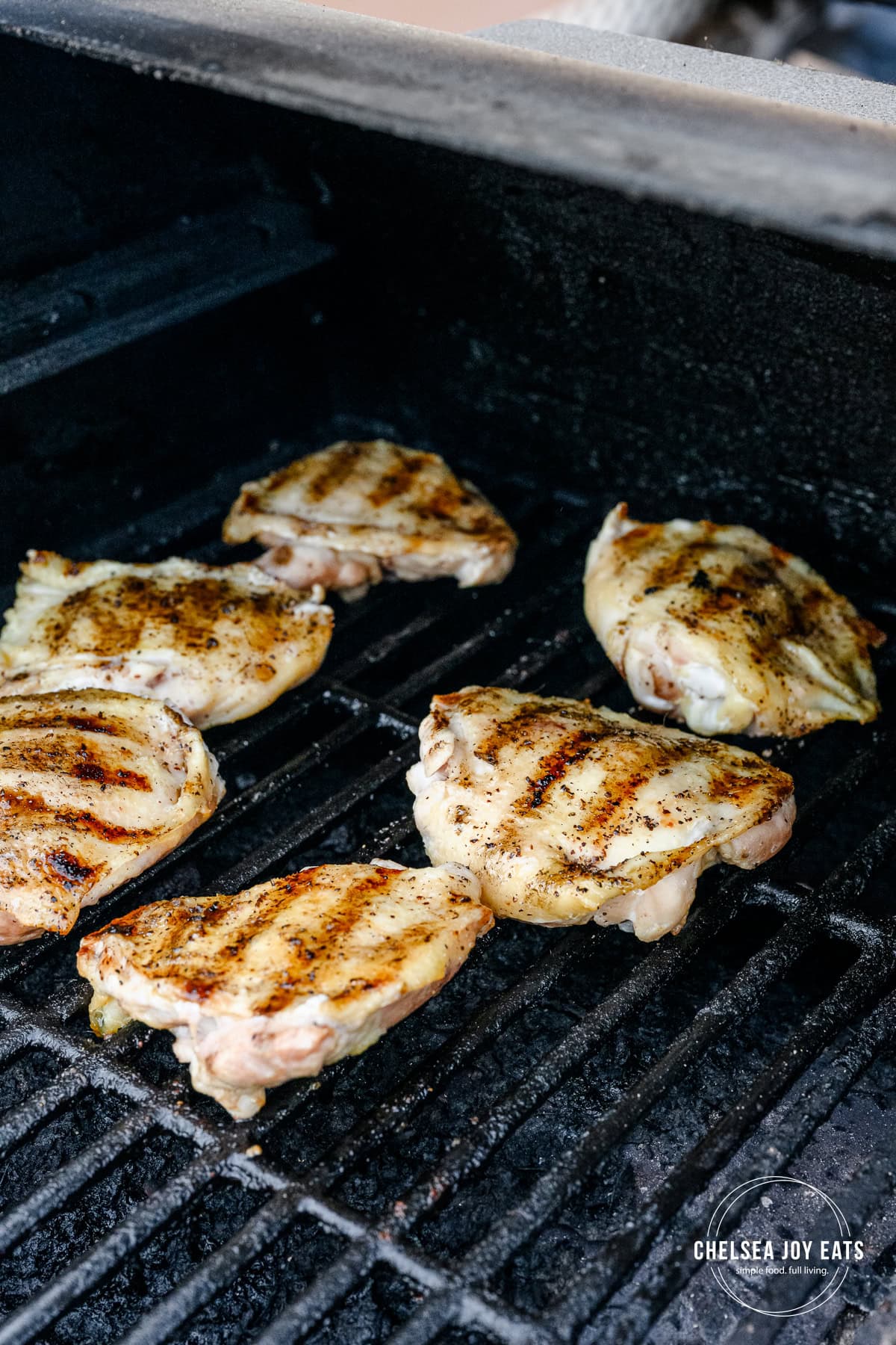 Chicken thighs cooking on a grill with grill marks on the visible skin side.