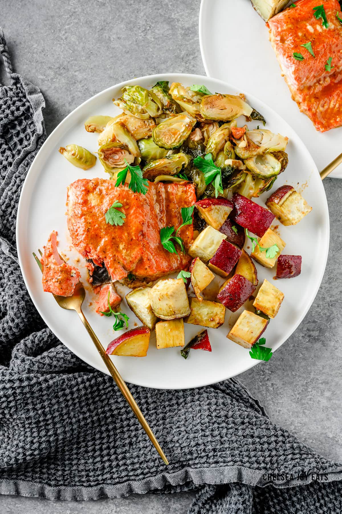 Roasted maple mustard salmon, sweet potatoes, and brussels sprouts on a white plate with a gold fork taking a bite.