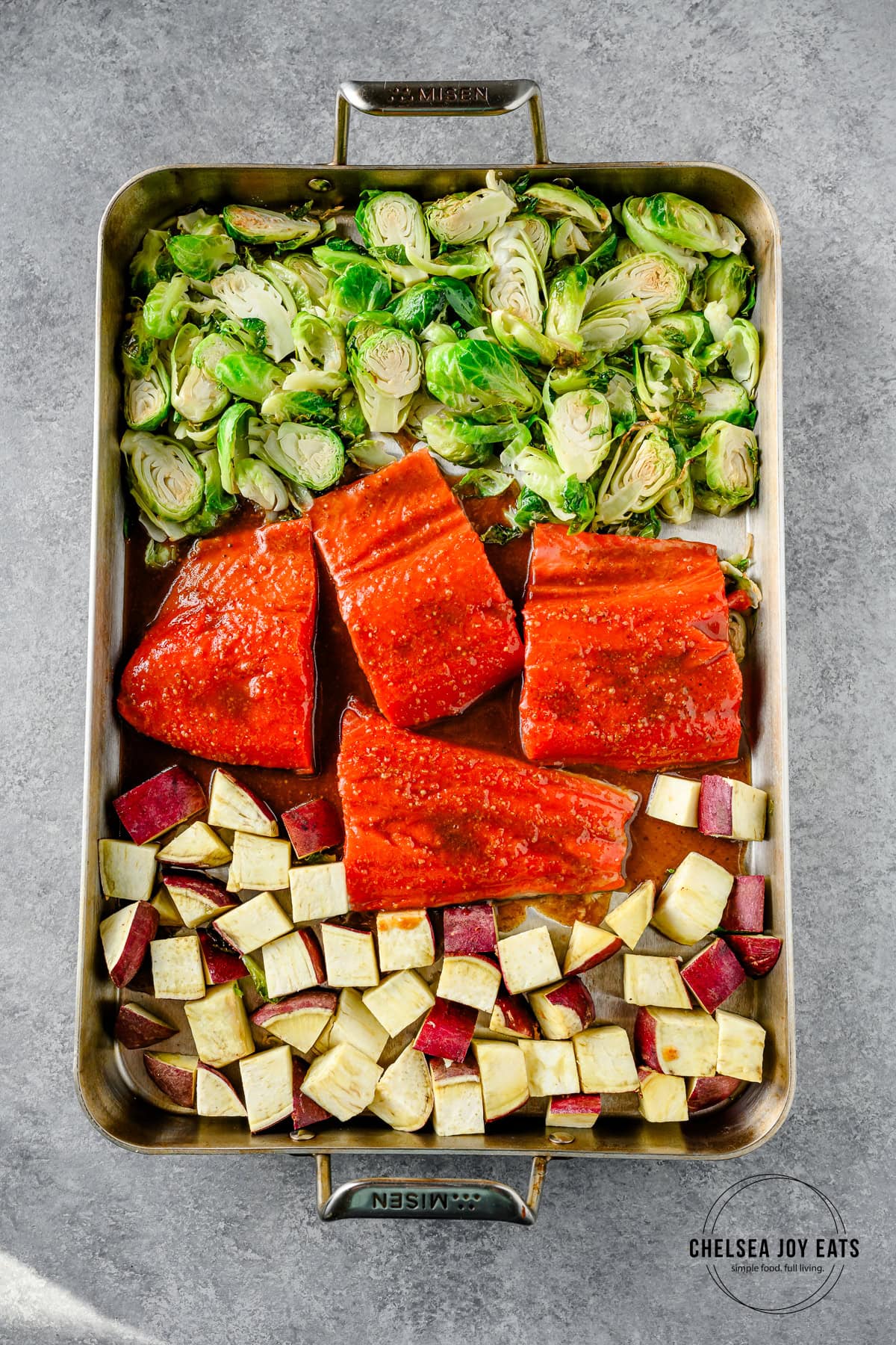 Maple mustard sauce drizzled over salmon fillets, brussels sprouts, and sweet potatoes on a sheet pan.