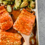 Roasted maple mustard salmon on a sheet pan with a spatula lifting a portion of salmon off the sheet pan.