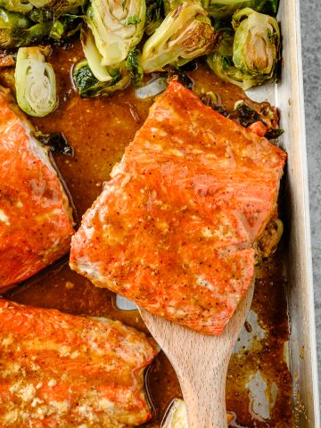 Roasted maple mustard salmon on a sheet pan with a spatula lifting a portion of salmon off the sheet pan.