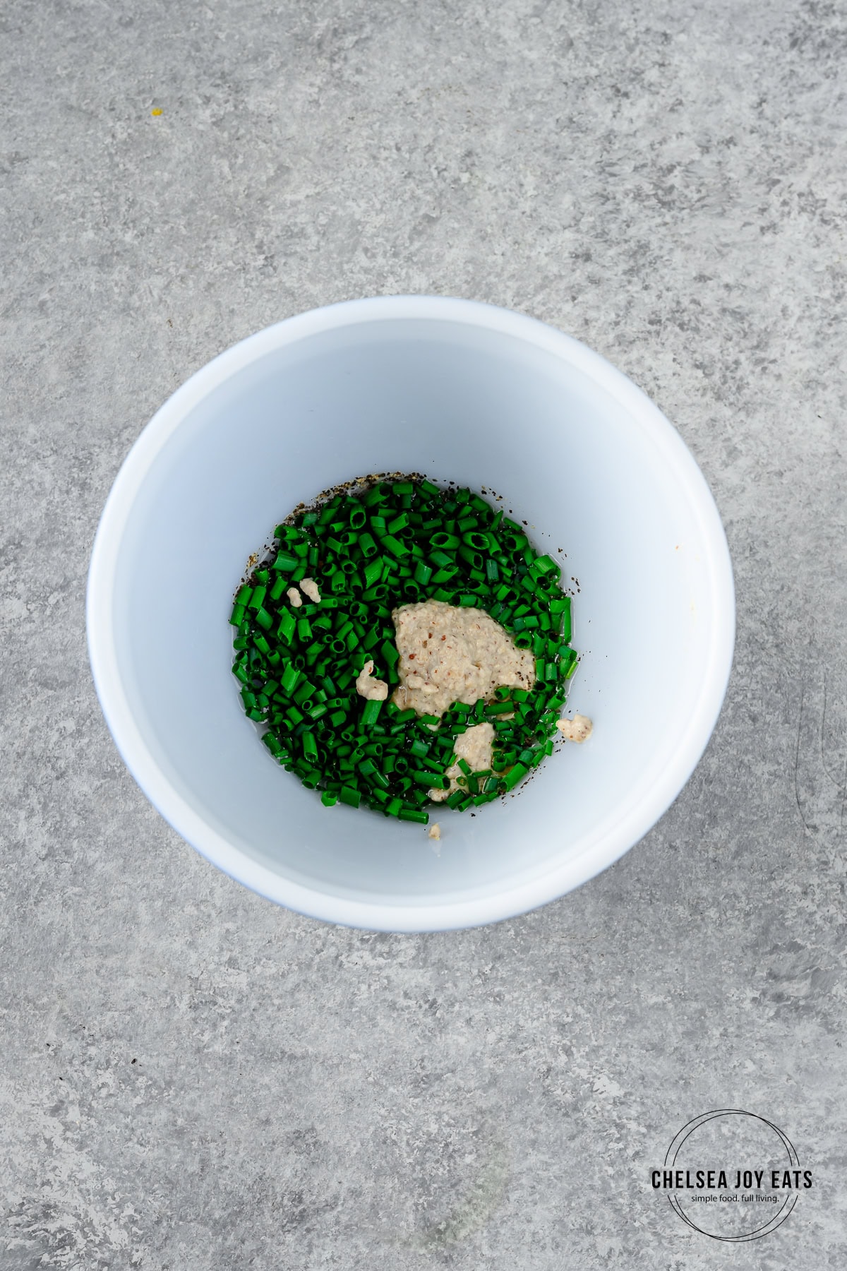 Small ceramic bowl with fresh chives, mustard, and lemon juice inside.