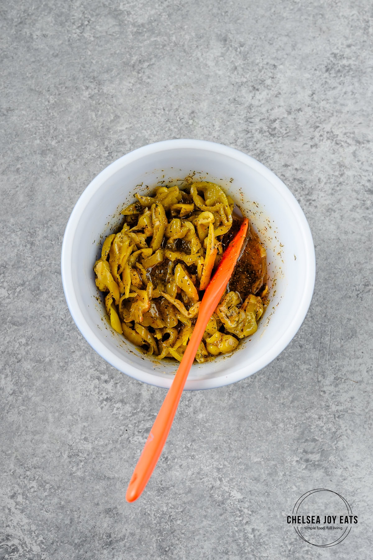 Pepperoncini, butter, and spices stirred together with a spatula in a small bowl.