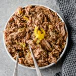 Bowl filled with pepperoncini shredded beef, garnished with pepperoncinis and dill, with two serving spoons.