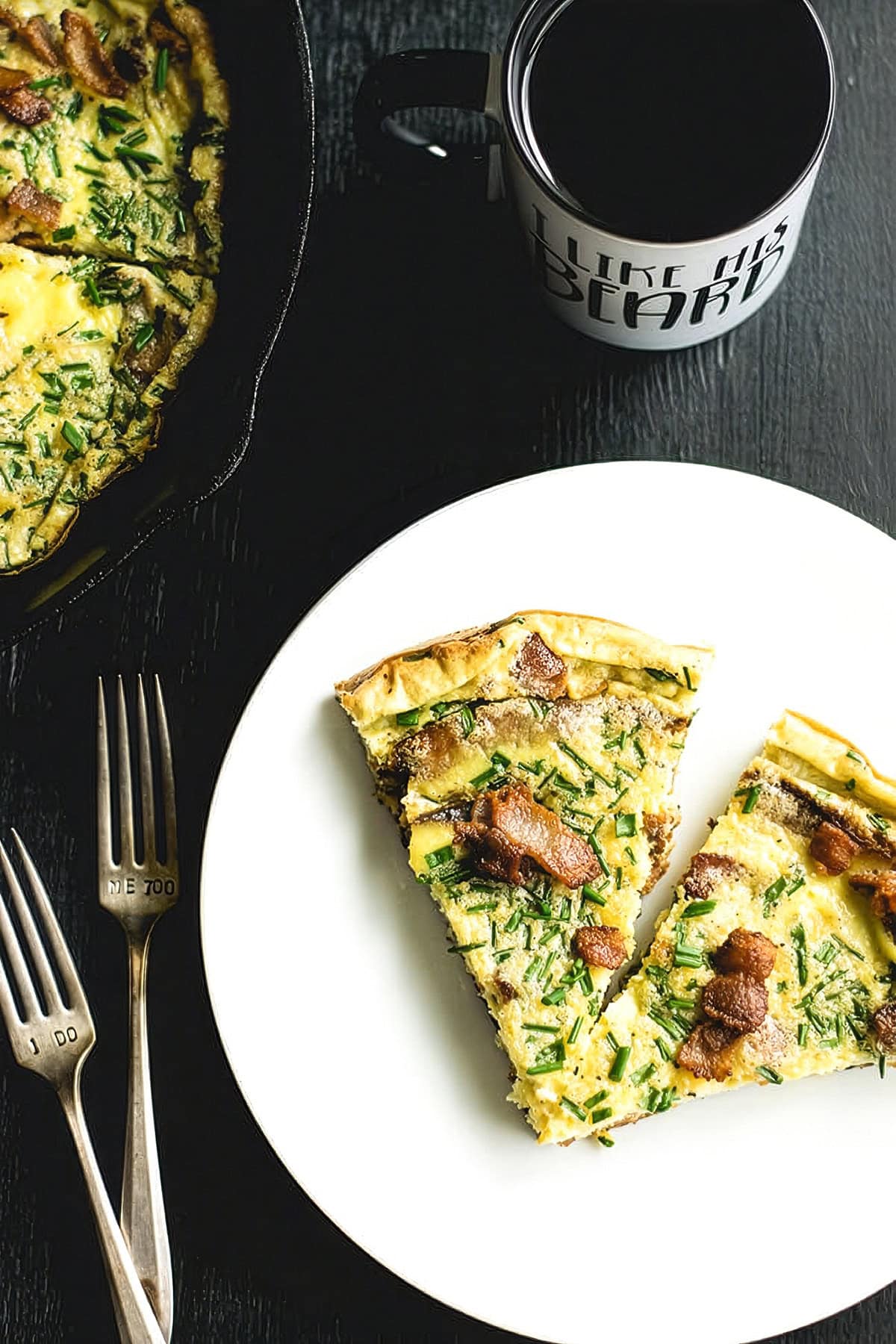 White plate with two slices of a plantain frittata with bacon and chives, with forks and a mug of coffee alongside.