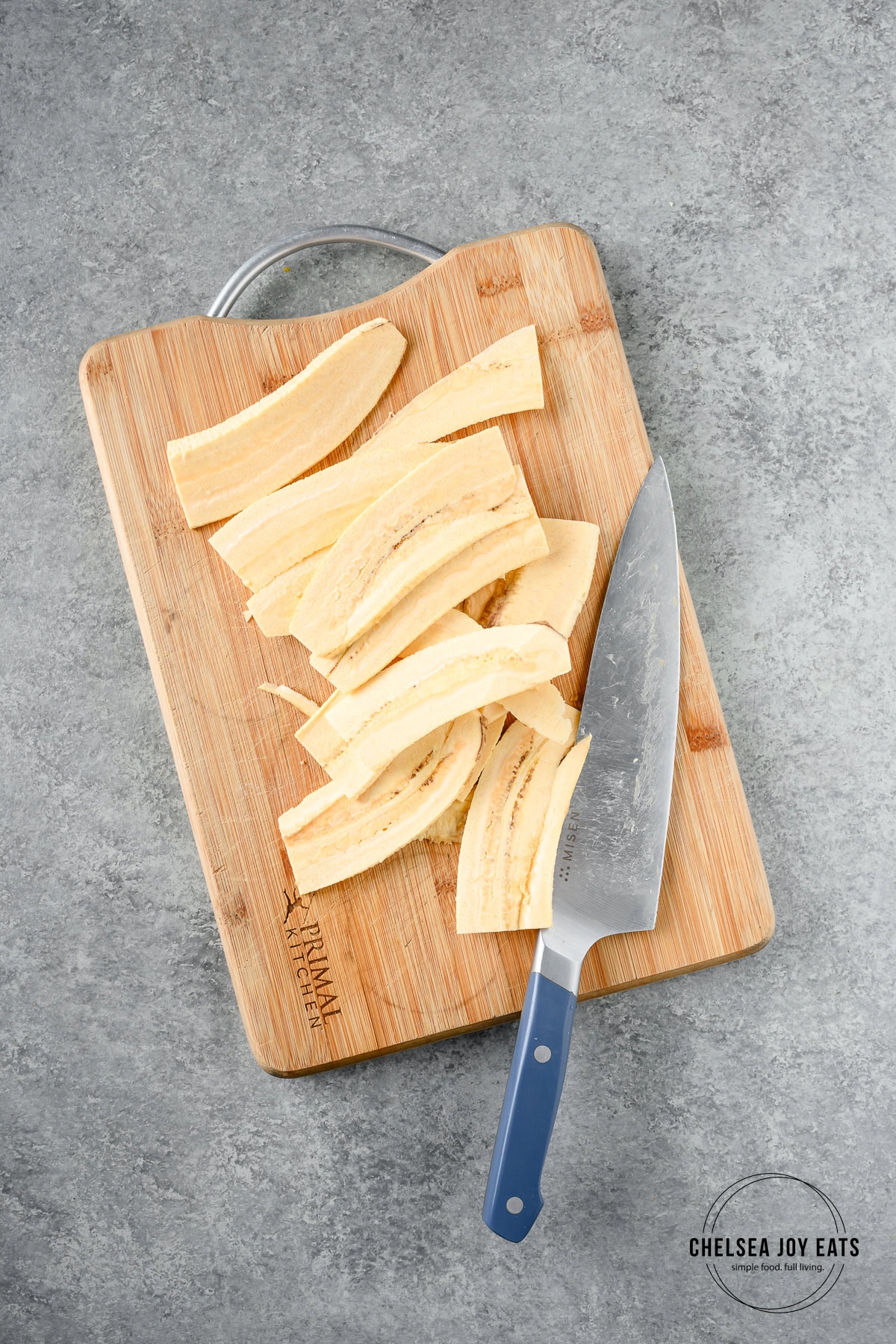 Peeled and sliced plantain on a cutting board with a chef's knife alongside.