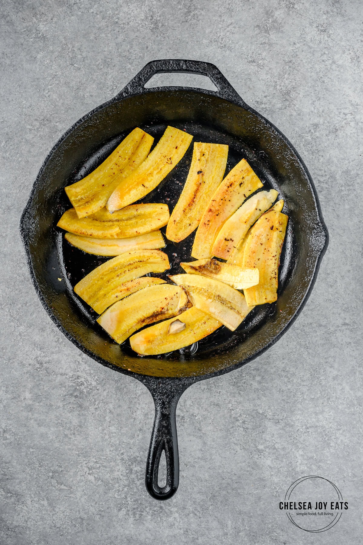 Plantain slices frying in bacon fat in a cast iron skillet.