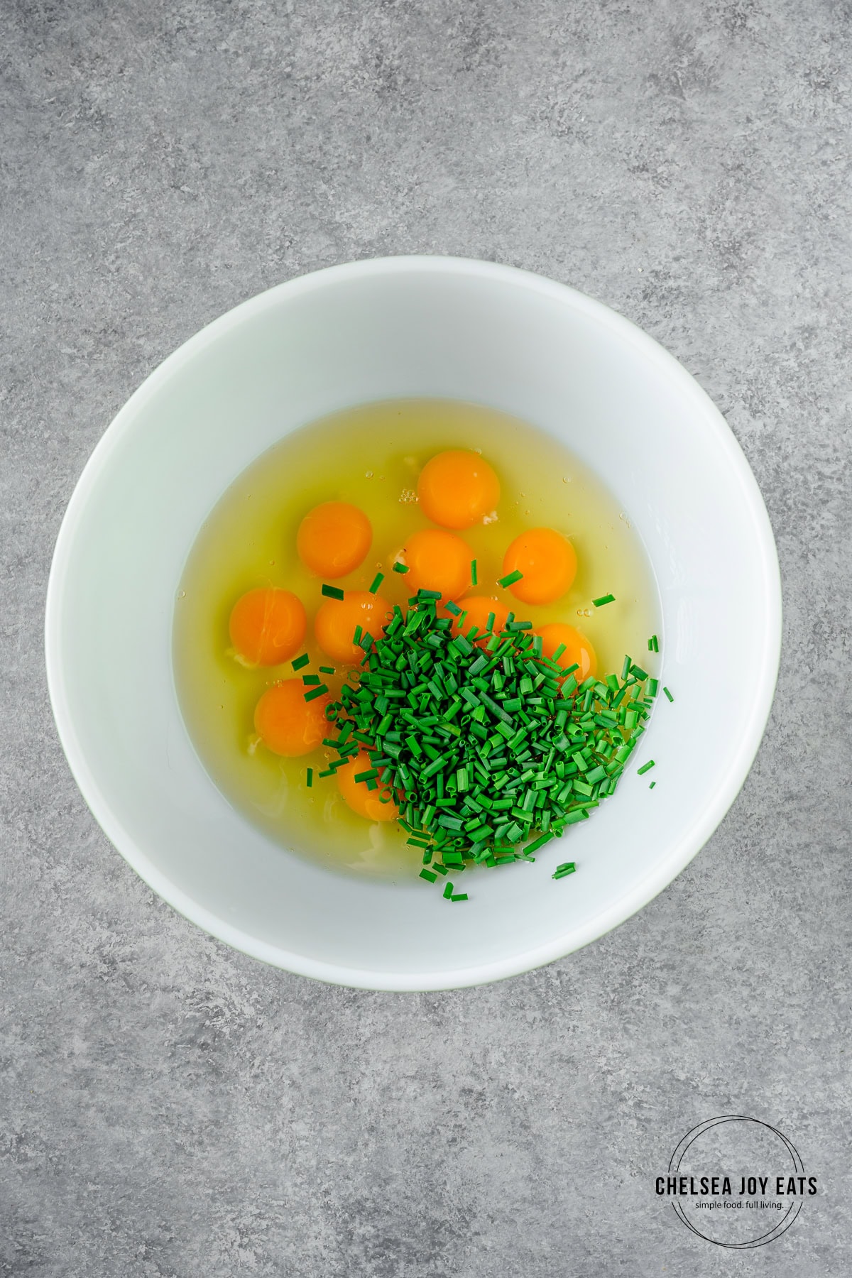 Unwhipped eggs and fresh chives in a large ceramic mixing bowl.