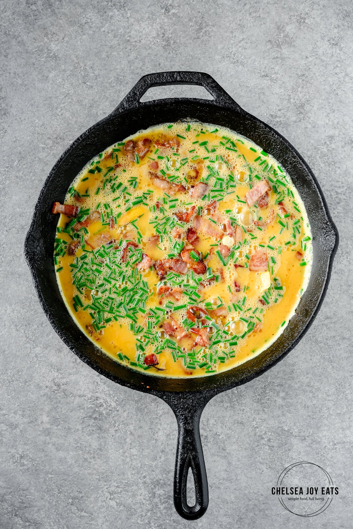 Uncooked frittata with plantain, chives, and bacon in a cast iron skillet.