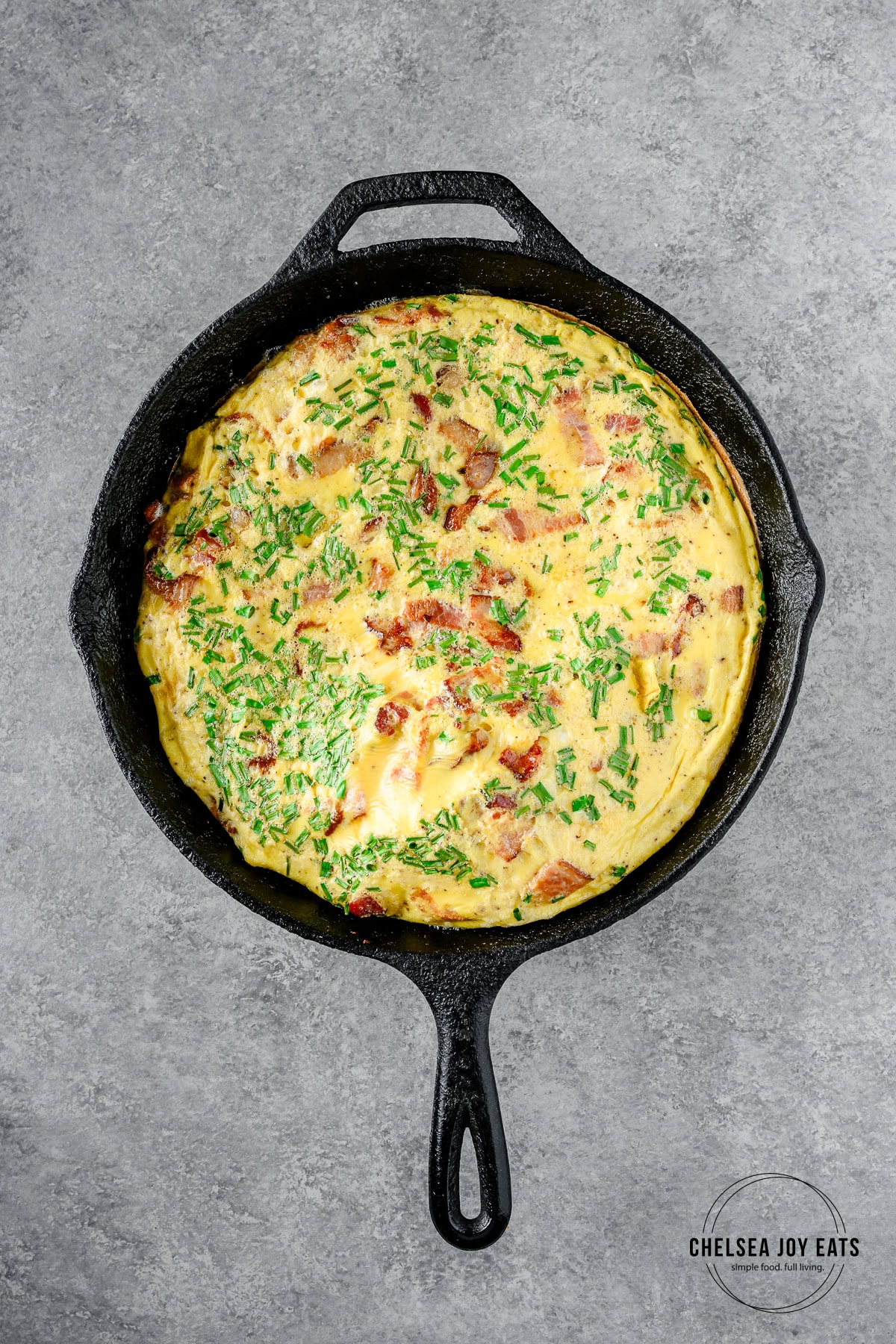 Cooked plantain frittata with chives and bacon in a cast iron skillet.