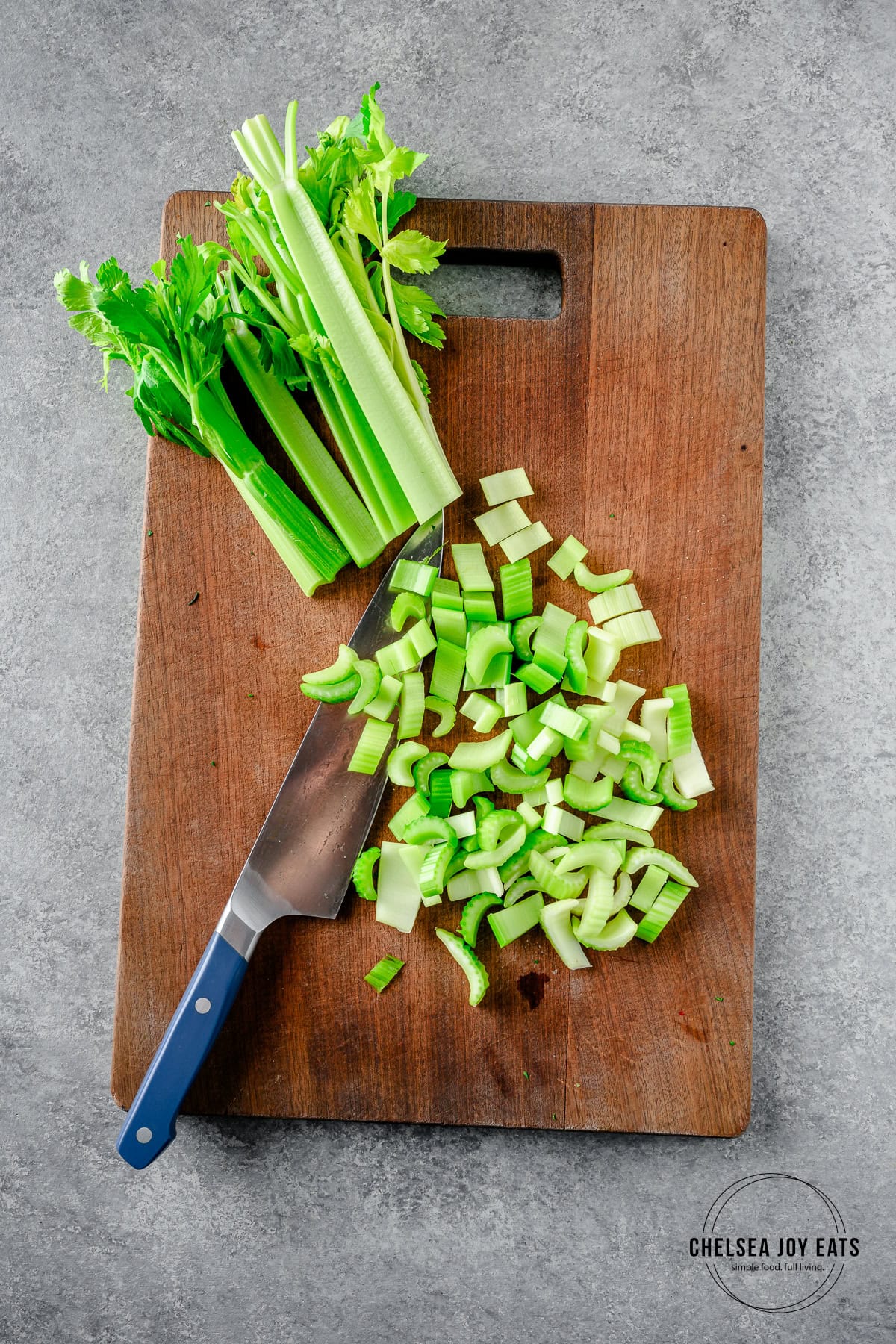 Stalks of celery half-chopped on a cutting board, with a knife alongside.