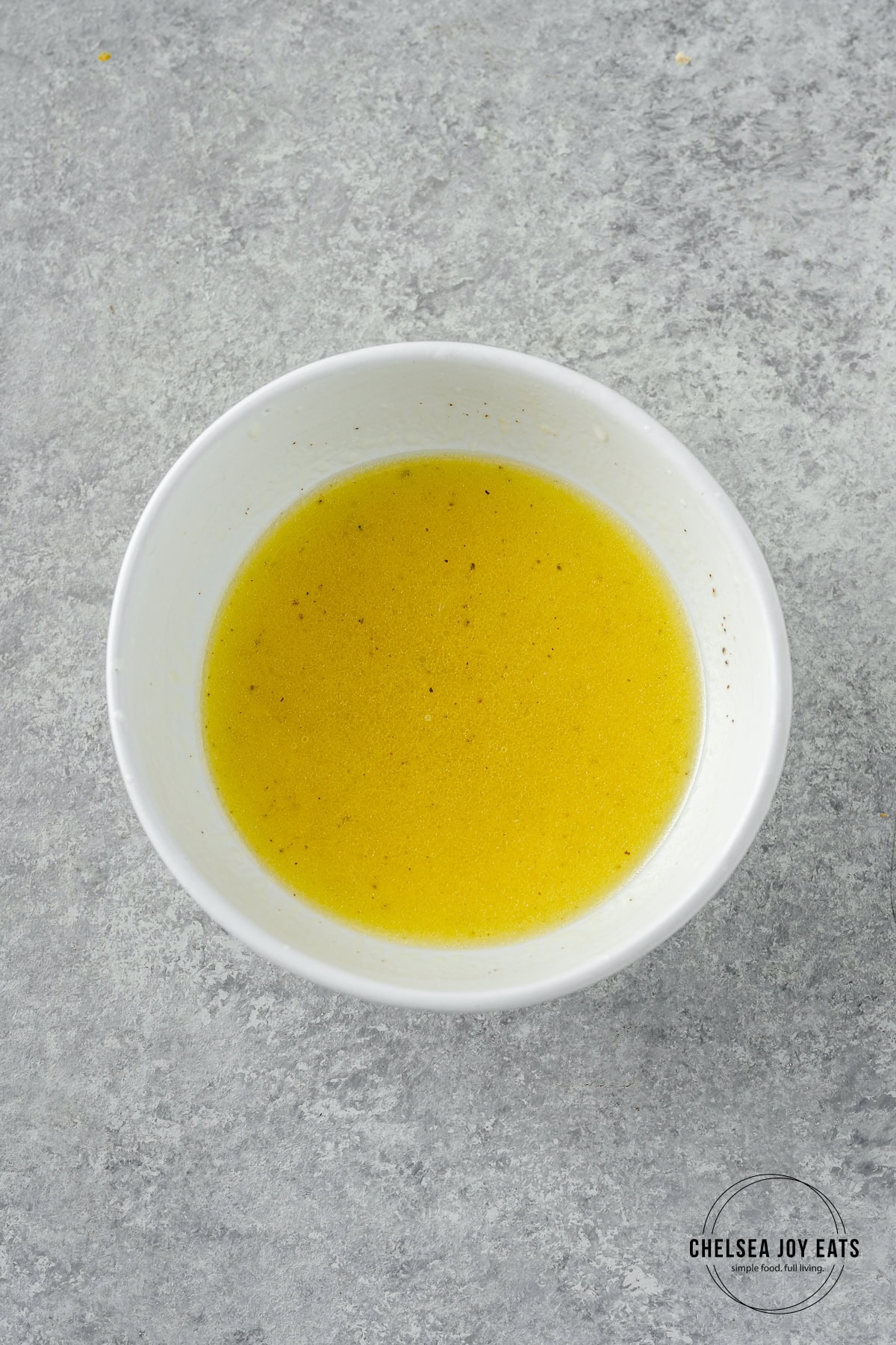 A small bowl of lemon vinaigrette on a marble background.