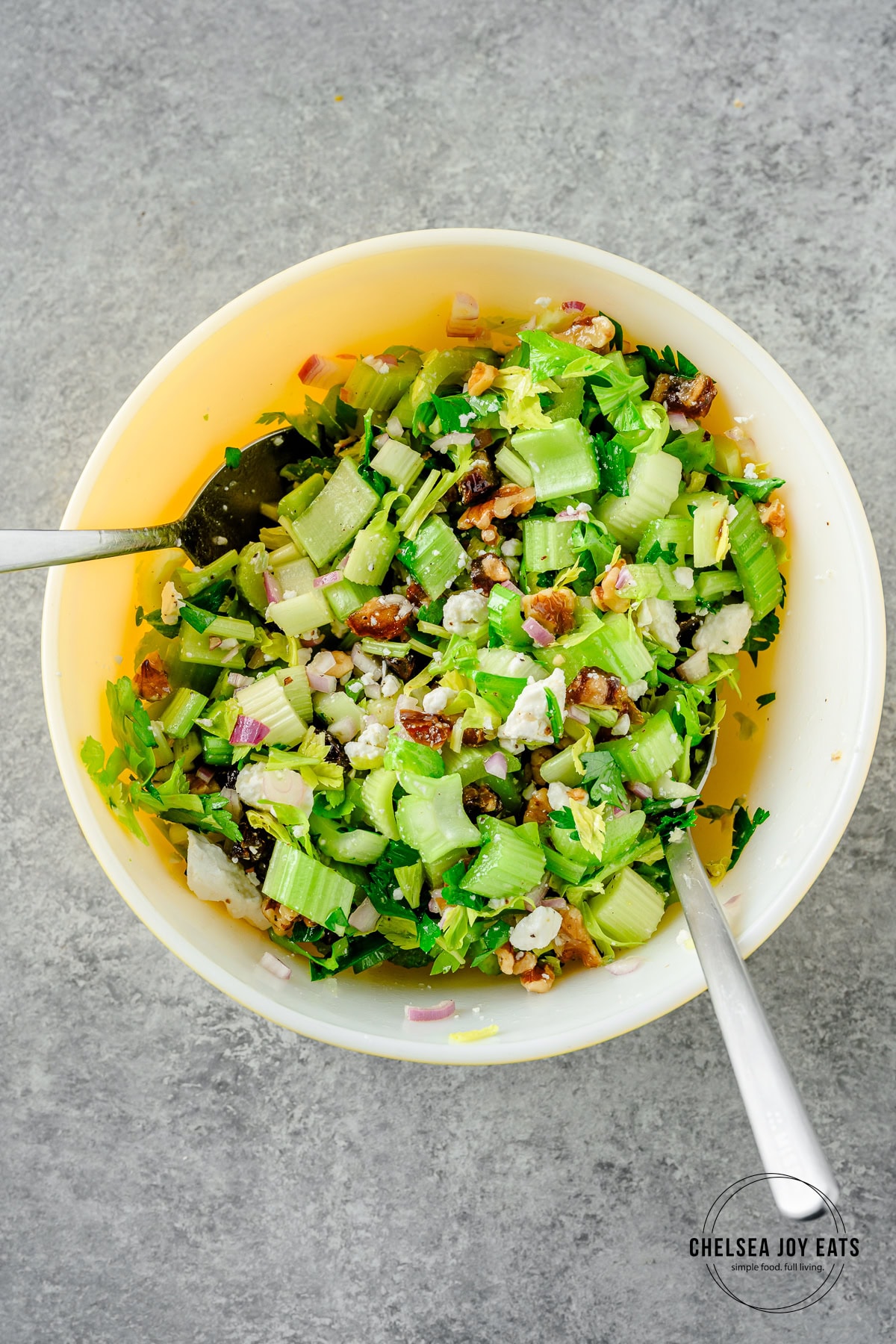 Dressed and tossed celery salad in a large ceramic bowl with two serving spoons.