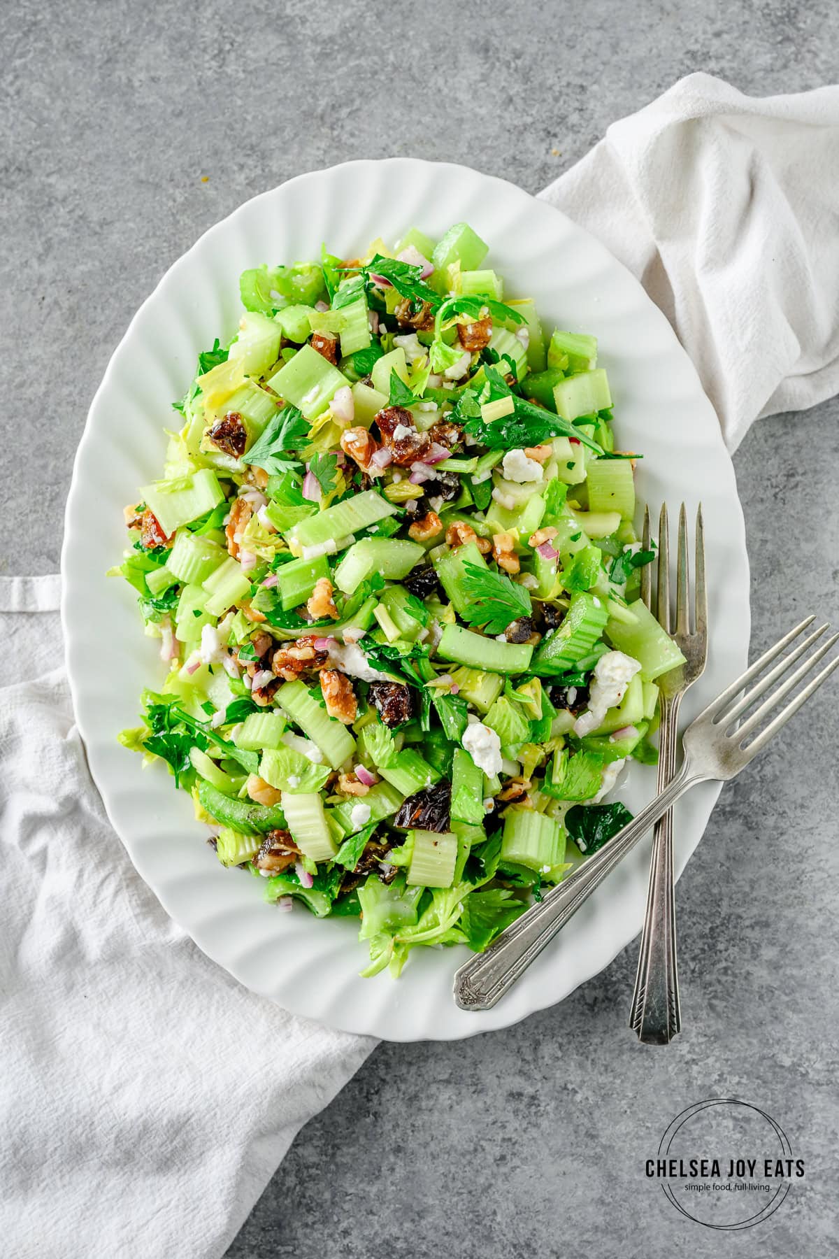 Fresh celery salad with dates, walnuts, and feta cheese on a white serving platter with two forks.