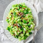 Fresh celery salad with dates, walnuts, and feta cheese on a white serving platter with two forks.