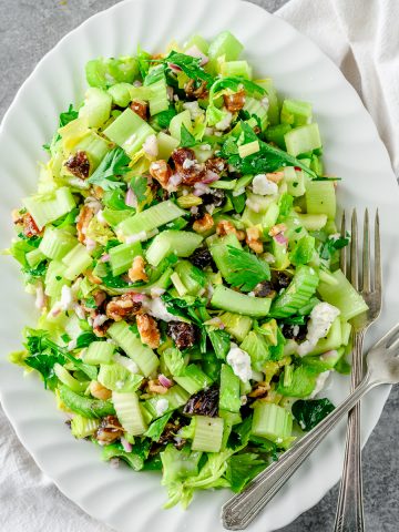 Fresh celery salad with dates, walnuts, and feta cheese on a white serving platter with two forks.