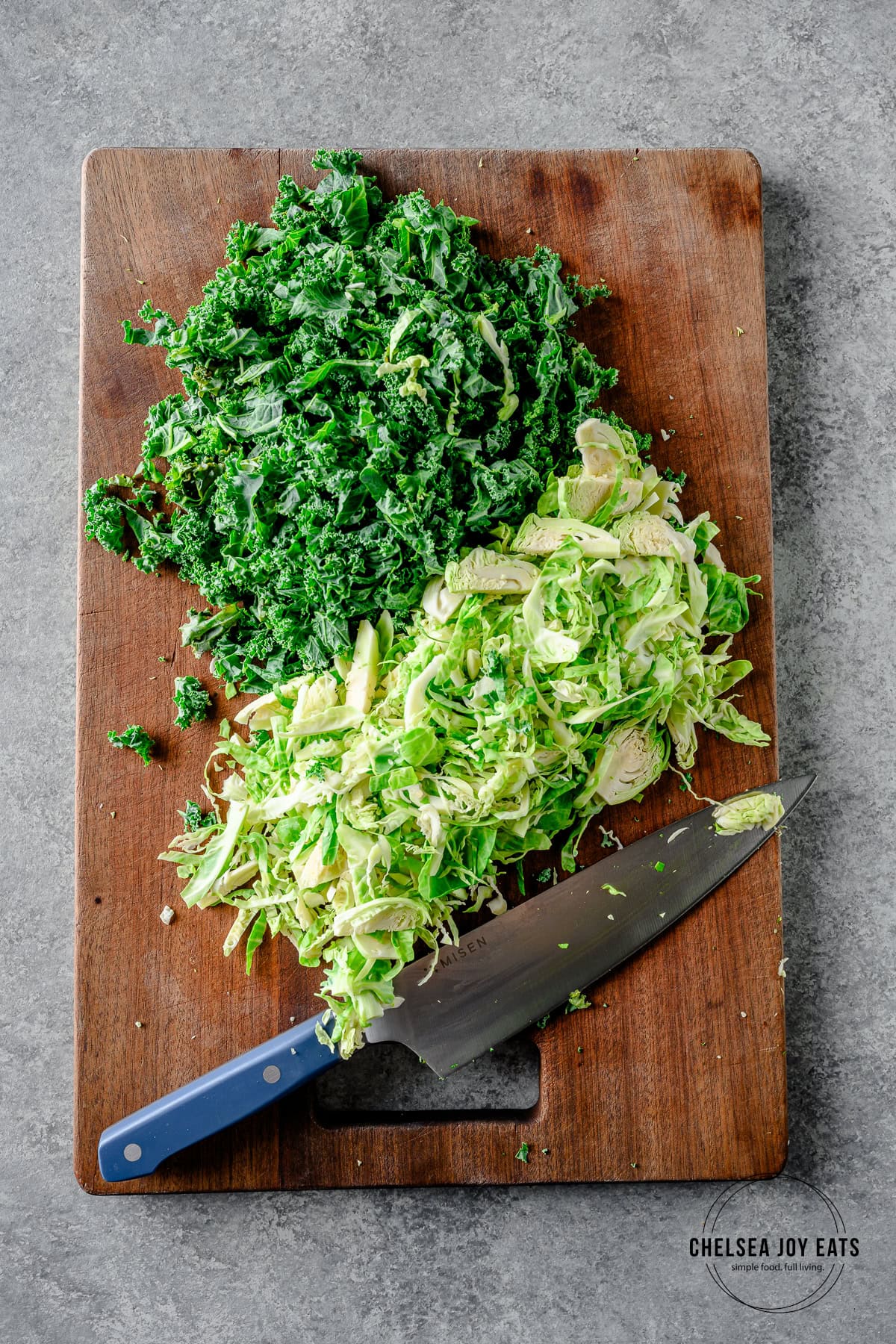 Finely chopped kale and brussels sprouts on a cutting board with a chef's knife.