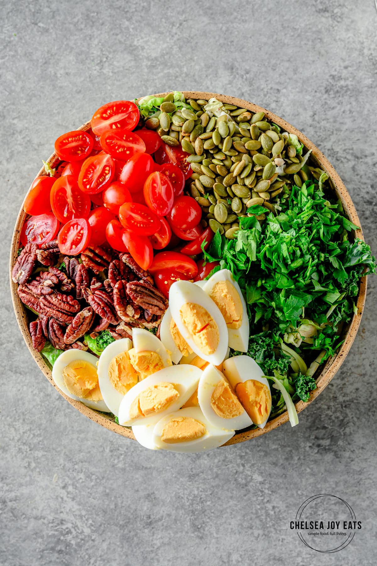 Assembled chopped brussels sprout and kale salad with hard-boiled eggs, parlsey, pepitas, tomatoes, and pecans.